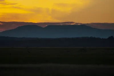 A stunning sunset over a silhouetted Alaskan mountain range, with vibrant orange and yellow light filling the sky.